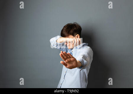 A woman covers her face and head with her hands, hides. Woman portrait on a gray background. Copy space. Stock Photo