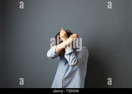 A woman covers her face and head with her hands, hides. Woman portrait on a gray background. Copy space. Stock Photo