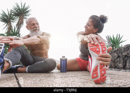 Happy fitness friends doing legs stretching exercises together in outdoor area - Sporty couple workout while laughing looking each other