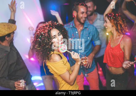 Group of friends dancing and drinking champagne at nightclub - Young happy people having fun and enjoying party eating candy lollipops Stock Photo