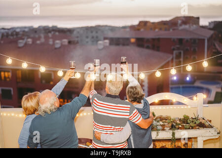 Happy senior friends cheering and toasting with red wine on rooftop - Mature people having fun and drinking at barbecue party in terrace Stock Photo