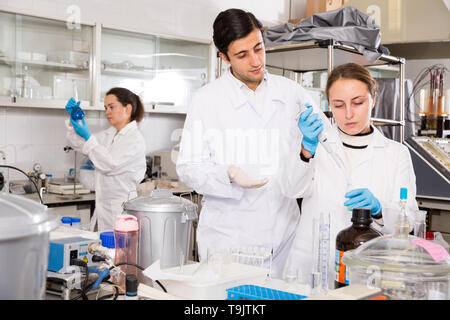 Two students performing experiments in university laboratory, using mechanical lab pipette for mixing chemicals Stock Photo