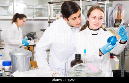 Two glad lab technicians discussing while working with reagents in test tubes during chemical experiment Stock Photo