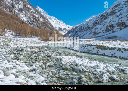 Prominent, snowcapped peak towers above the valley. Swiss Alps. Snow-covered valley, glacial-fed river, fresh snow on the river bed rocks.
