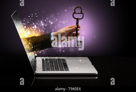 Hand with huge vintage key coming out of a laptop with sparkling effects  Stock Photo