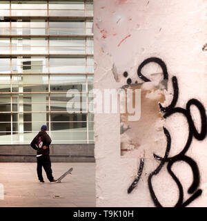 Back view of a young skateboarder standing and relaxed in front of Macba, museum in Barcelona. The boy tipping up the skateboard with his foot. Graffi Stock Photo
