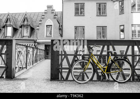 A picture of a lonely yellow bike standing in the typical street in Stockholm by the bridge to a house. The bike looks to be modern in a retro style. Stock Photo