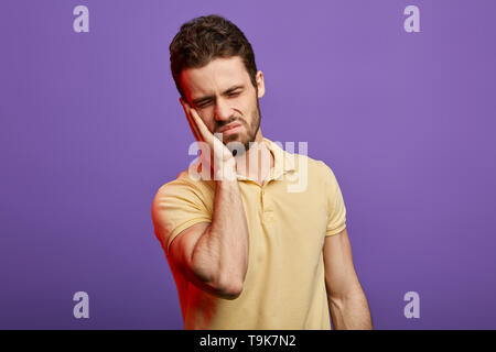 emotional handsome man feeling pain, holding his cheek, suffering from bad toothache. illness, tooth decay, cracked enamel, cavities, infection Stock Photo