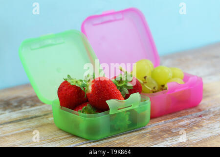 Fresh strawberries and sweet grapes in colorful plastic boxes on rustic wooden surface