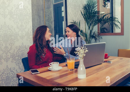 Two excited women reading online good news on a laptop while sitting in cafe - Image Stock Photo