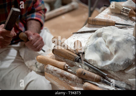 Sculptor working on alabaster sculpture in his workshop with hammer and chisel. Various tools on the bench. Stock Photo