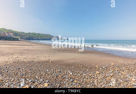 Sandsend near Whitby. Old wooden breakwater posts lead down from the beach and a headland is in the distance. Colourful pebbles are in the foreground. Stock Photo