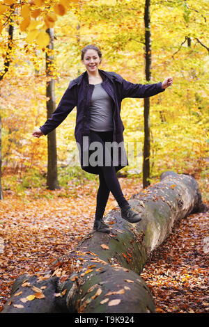 happy carefree young woman balancing on tree trunk in forest - enjoying active lifestyle in fall season