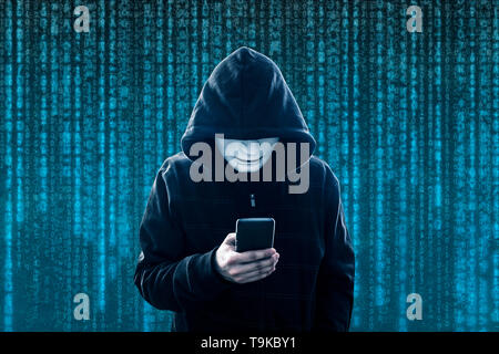 Hooded hacker with mask holding smartphone Stock Photo