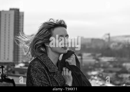 A sad and unhappy woman stands on the edge of the roof of a high-rise building. Stock Photo