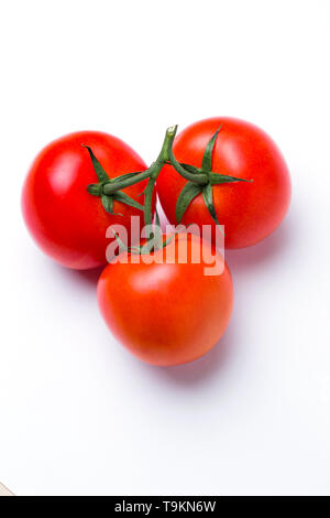 Closeup of three red fresh tomatoes in a pile in a green stalk on white isolated background, top view. Healthy diet, vegetarian food Stock Photo