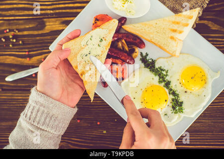 Girl smears butter with a knife on a triangular fried toast. Breakfast of fried eggs with toast Stock Photo