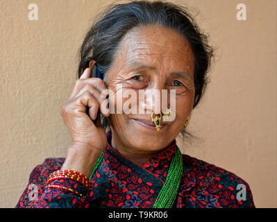 Elderly Nepali Gurung woman with elaborate nose jewelry makes a call on her cell phone. Stock Photo