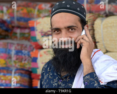 Indian Rajasthani Muslim cloth merchant with black Islamic beard wears a religious skull cap (taqiyah) and makes a call on his cell phone. Stock Photo