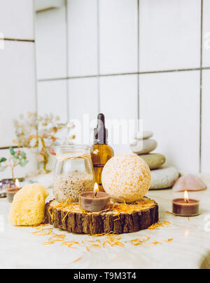 Side view of home wellness spa products, orange bath bomb, aroma bath salt, sea sponge, tea candles lit. Very zen set, tree of love and amethyst cryst Stock Photo