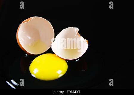 Close up of brown cracked egg shell with raw yellow yalk and slimy egg white on reflecting shiny black background Stock Photo