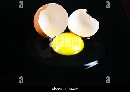 Close up of brown cracked egg shell with raw yellow yalk and slimy egg white on reflecting shiny black background Stock Photo