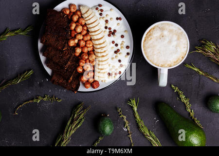 Top view of healthy Breakfast, a Cup of latte or coffee, cocoa, avocado, feijoa, rosemary, cumin on a black background, close up, flat lay Stock Photo
