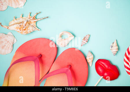 Bright flip flops with seashells and red lollipops in shape of lips on mint background. Flat lay composition. Beach, summer, holiday, sea, vacation co Stock Photo