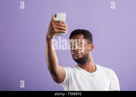 Portrait of confident attractive friendly african american student with short curly hair and beard wearing white t shirt holding mobile phone taking s Stock Photo