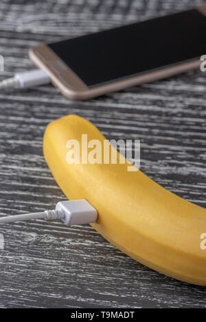 Touchscreen smartphone is connected to a fresh juicy banana with a white usb cable. The concept of measuring the useful properties and qualities of fo Stock Photo