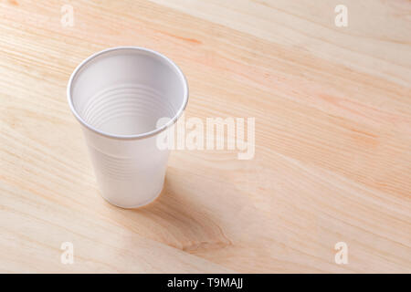 White plastic Cup stands on a wooden table of natural color. the concept of abandonment of plastic utensils Stock Photo