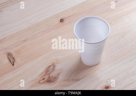 White plastic Cup stands on a wooden table of natural color. the concept of abandonment of plastic utensils Stock Photo