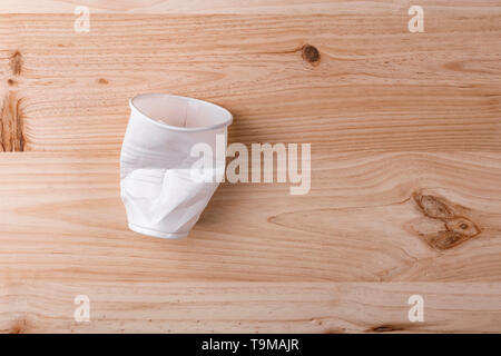 Broken crumpled white plastic Cup lies on a wooden table of natural color. the concept of abandonment of plastic for nature conservation Stock Photo