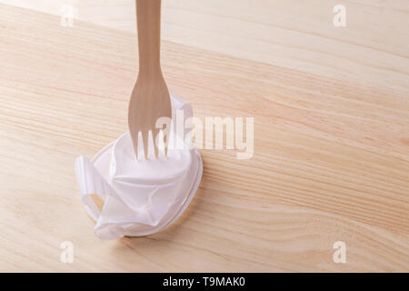 White plastic cup crumpled with a wooden eco fork on the wood table. The concept of rejection of plastic utensils and environmental protection Stock Photo