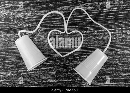 Phone made of white plastic cups and white rope laid in the form of a heart on a black wooden table Stock Photo