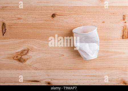 Broken crumpled white plastic Cup lies on a wooden table of natural color. the concept of abandonment of plastic for nature conservation Stock Photo