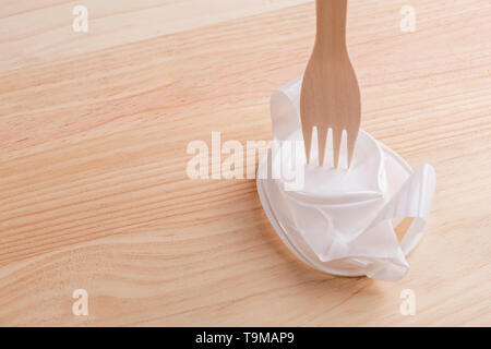 White plastic cup crumpled with a wooden eco fork on the wood table. The concept of excellence eco products over plastic Stock Photo