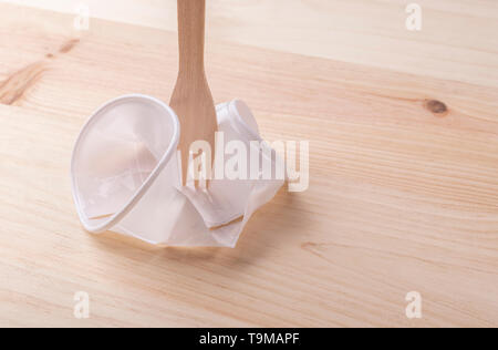 White plastic cup crumpled with a wooden eco fork on the wood table. The concept of excellence eco products over plastic Stock Photo
