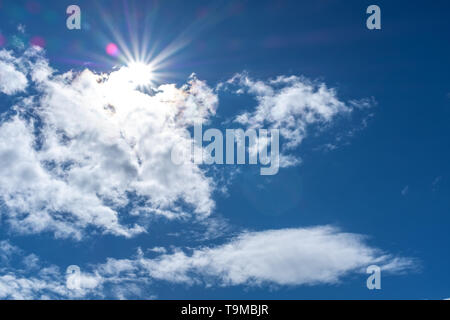 Cloudscape with a sun star appearing from behind against a blue sky Stock Photo
