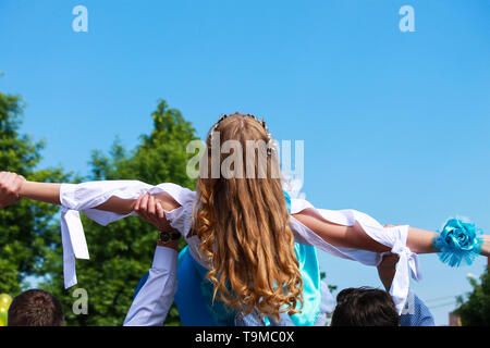 The blond girl in the white-blue dress on the raised male hands while dancing. Wedding, birthday, graduation. holiday, spring and summer Stock Photo