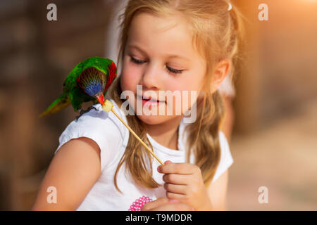 Cute little girl playing with a parrot and feed him Stock Photo