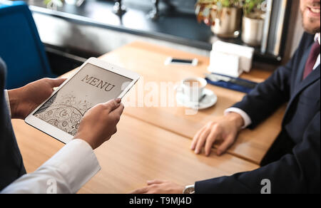Young waitress with menu on tablet PC screen in restaurant Stock Photo