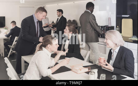 Cheerful multinational colleagues having break at office, drinking coffee and talking Stock Photo
