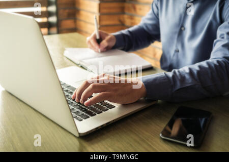 Businessman typing in information on a laptop or browsing the internet as he makes notes in a journal on the desk Stock Photo