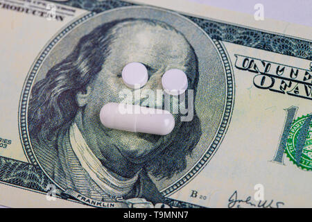 A pills lie in place of the eyes, on a bill of one hundred dollars close-up. The concept of insurance medecine, high cost, high cost of drugs. Costly treatment. Stock Photo