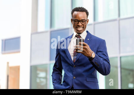 Outdoor standing portrait of a black African American business man using a mobile  phone Stock Photo