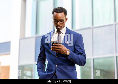 Outdoor standing portrait of a black African American business man using a mobile  phone Stock Photo