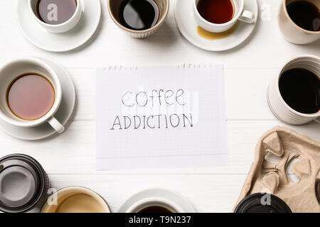 Almost empty cups of coffee and paper sheet with text COFFEE ADDICTION