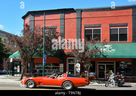 A causcasion man in a red corvette convertible drives in downtown Coeur d'Alene, ID,  alongside the Moose Market and lounge in vintage red and black b Stock Photo