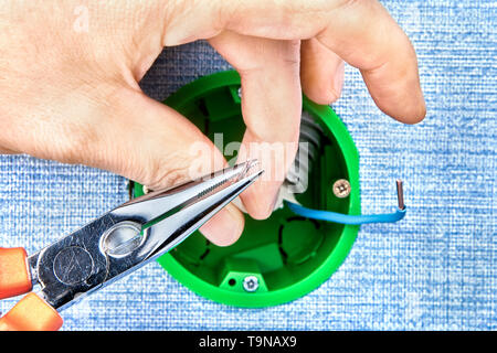 Worker is cutting copper wires inside round electrical box with help of long nose pliers, electrical work. Stock Photo
